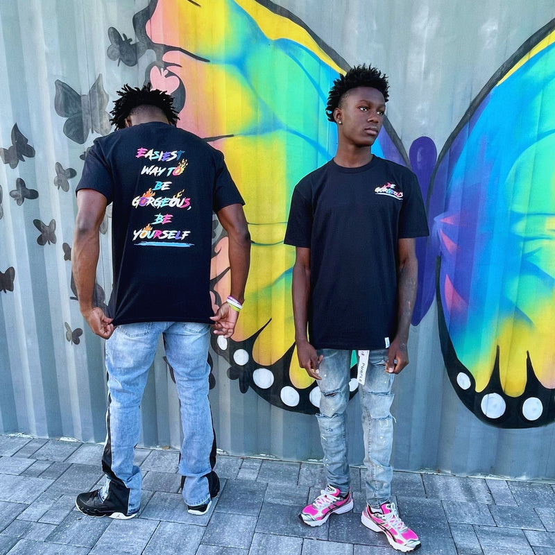 Two people standing in front of a colorful butterfly mural.