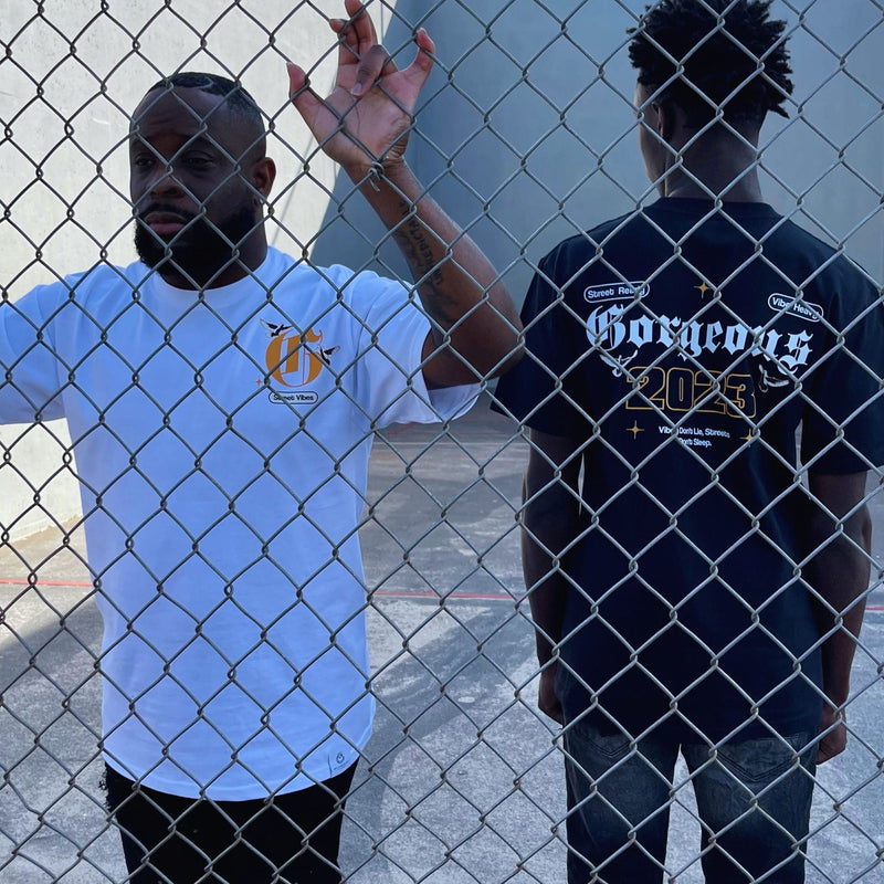 Two people standing behind a chain-link fence, wearing Street Vibes t-shirts.